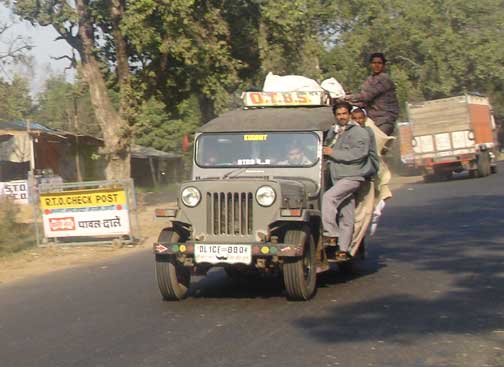 Jeep with three men riding on the running board.